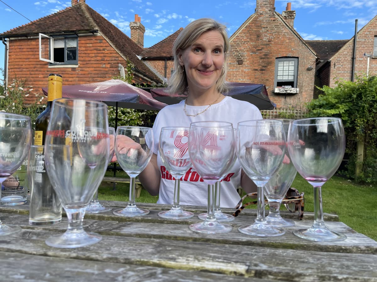 A woman sitting among wine glasses in a garden